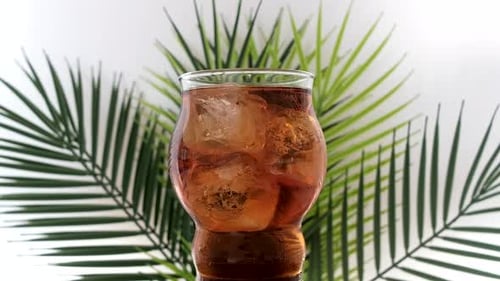 Iced drink in clear glass with tropical background