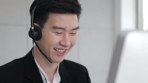 Asain call center wear headset and working with computer while consulting customer