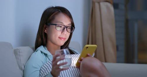 Woman on Couch Using Phone and Drinking Water