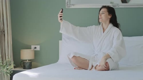 Woman in Bathrobe Video Chatting on Bed