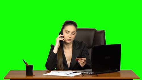 Woman at the Workplace Takes a Credit Card and Call on the Phone. Green Screen. Studio