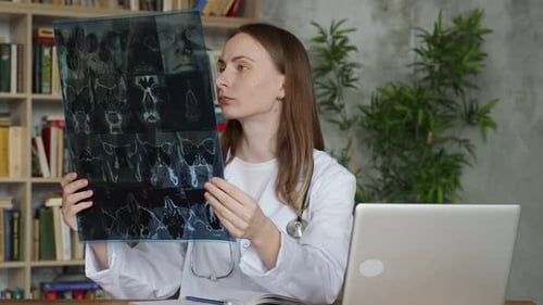 A Young Female Doctor Looks at an Xray While Sitting in an Office in a Clinic