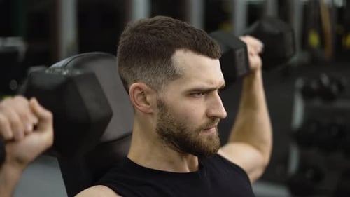 Stark fitter Mann beim Sitzen beim Hanteldrücken während des Trainings auf einer Bank