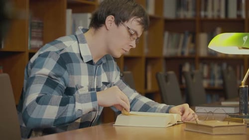 Portraitaufnahme des Mannes, der ein Buch in der Nähe des Bücherregals in der Bibliothek liest