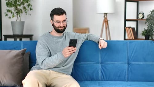 Man Using Phone Relaxing on Sofa at Home