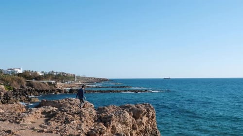 Attractive young boy running to edge of cliff and raising hands to sky showing victory and success