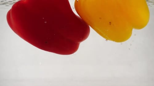 Red and Yellow Bell Peppers Falls Into Water with Splashes and Bubbles, Slow Motion Close-up