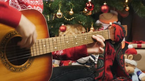 Guitarist Plays Acoustic Guitar by Christmas Tree