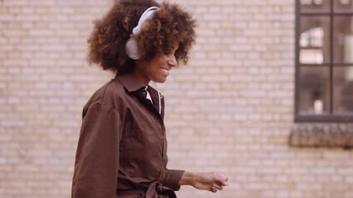Young Woman Moving To Music Through Headphones As She Moves Down Street