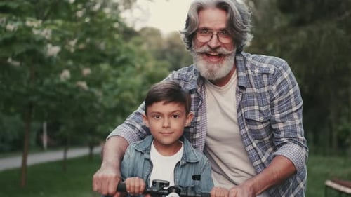 Smiling Boy on a Bike and Hippie Grandfather Standing in a Park