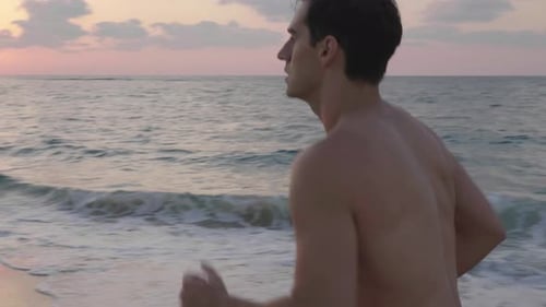 Handsome athletic man running on beach during sunset
