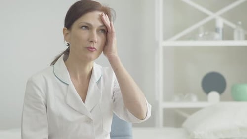 Worried Woman Rubbing Forehead in White Medical Office