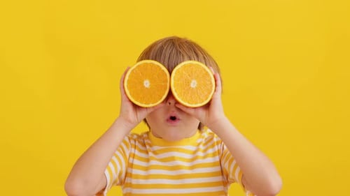 Boy with Orange Halves Over Eyes Against Yellow Backdrop