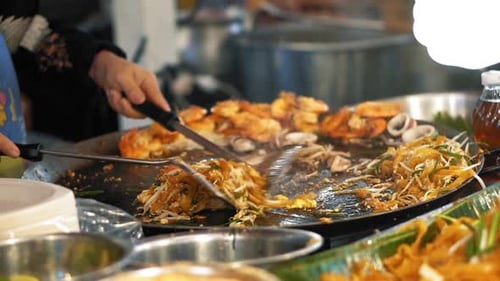 The chef prepares a yummy Pad Thai with tasty fried shrimp on an open wok
