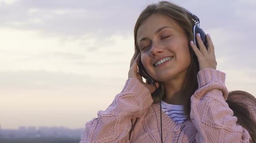 Smiling Woman Listening to Music With Headphones Outdoors