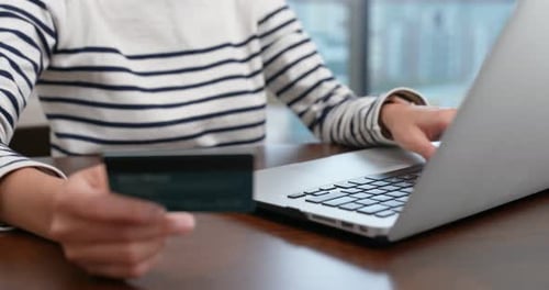 Woman Types on Laptop Holding Credit Card Indoors
