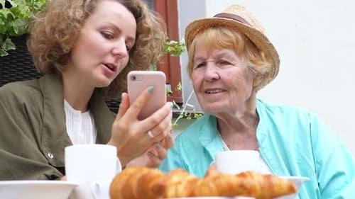 Granddaughter And Grandmother Using Smartphone In Cafe