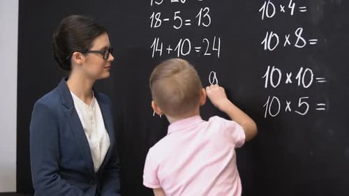 Écolier intelligent résolvant des exercices de mathématiques sur tableau noir, professeur debout près