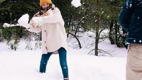 Woman Throwing Snowball in Winter Forest with Friend