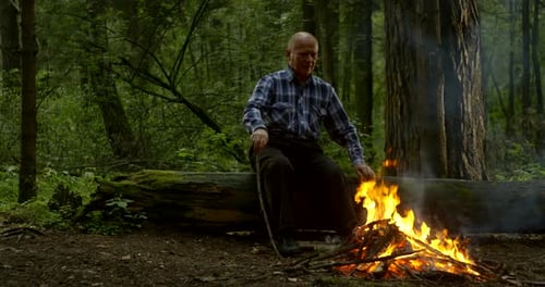 Alter Mann bewegt Zweige im Feuer und legt Kopf auf Hand
