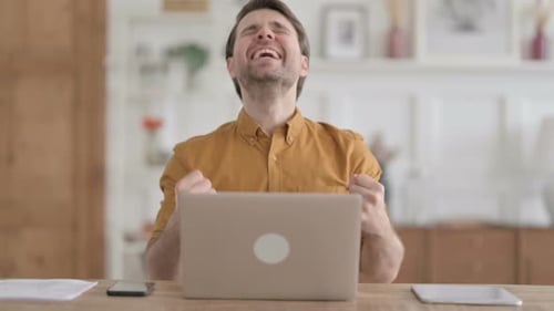 Young Man Celebrating Success while using Laptop in Office