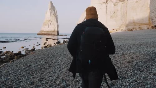Rear View Happy Traveler Man with Backpack Walks Along Sunny Rocky Sea Shore Cliffs Near Etretat