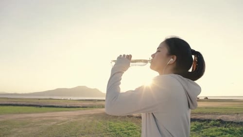 Woman Drinking Water During Outdoor Exercise at Sunset