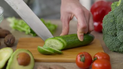 Closeup Woman Slicing Cucumber with Knife on Cutting Board in Kitchen