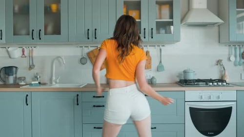 A Beautiful Woman in White Shorts is Relaxing at Home Dancing in the Kitchen