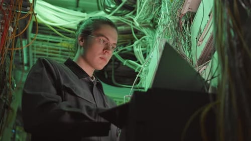 Young Adult Working in Server Room on Laptop