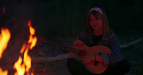 Young Woman with Guitar Beside Campfire at Night