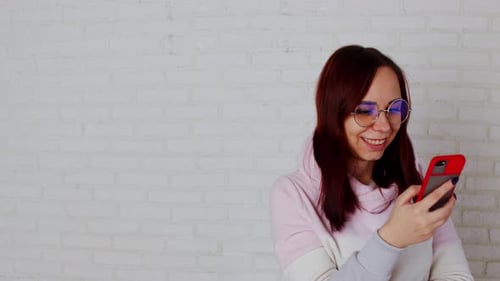 Woman Smiling at Phone in Front of Brick Wall