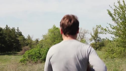 a Young Caucasian Man in Light Sportswear Runs in a Green Park