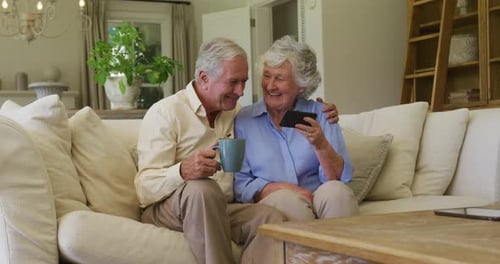 Senior Couple Smiling Together at Mobile Phone on Sofa