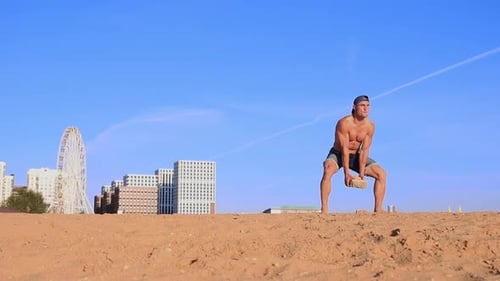 Young Fit Man Doing Sports Exercises at the Beach Raising Heavy Rock in His Hands