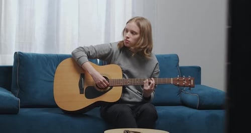 Woman Playing Acoustic Guitar on Blue Couch Indoors