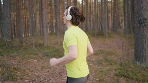 Young Man in Wireless Headphones Runs Through Pine Forest