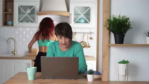 Senior Woman Stressed by Laptop While Woman Dances