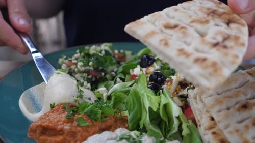 Person spreading hummus on flatbread with salad