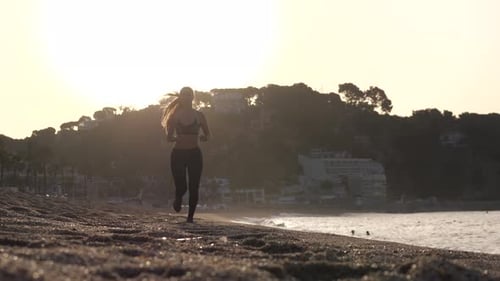 Sporty Female Running Along Sandy Beach at Sunrise