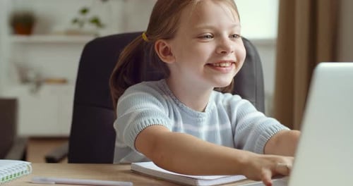 Nette kleine Tochter im Vorschulalter mit aufgeregten Gesichtsausdrücken beim Spielen von Online-Spielen auf Laptop
