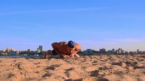Young Man Doing Push Ups at the Beach Leaning on the Rock