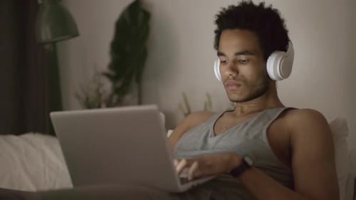 Young Adult Working on Laptop with Headphones at Night