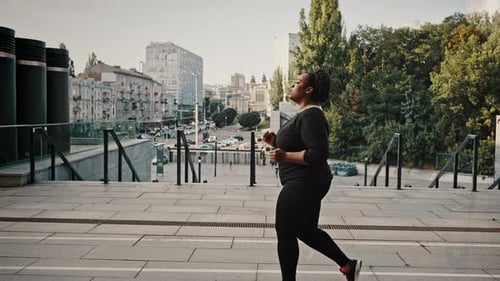 Side View Portrait of Young Overweight African American Woman Jogging Alone in Urban Park Practicing