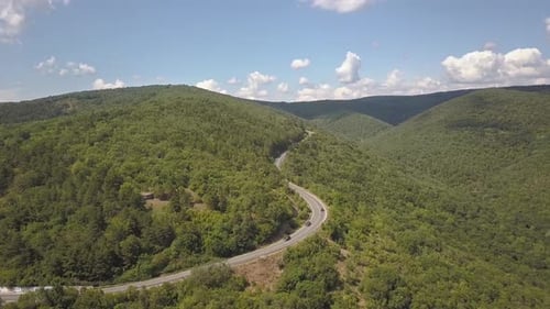 Aerial view of winding road with mowing cars and trucks in high mountain pass trough dense woods