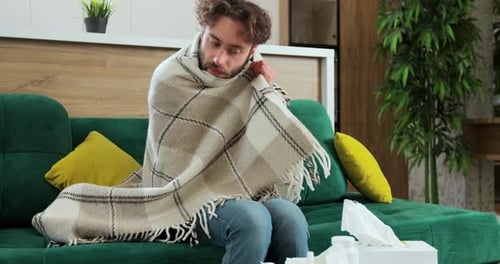 Recouvert d'un plaid tricoté chaud, malheureux et stressé, jeune homme frissonnant à cause de la basse température