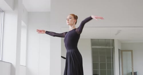 Caucasian female ballet dancer practicing ballet during a dance class in a bright studio