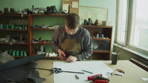 The Shoemaker in the Workshop Produces Handmade Leather Products. Cuts Out Shoe Shapes with Scissors
