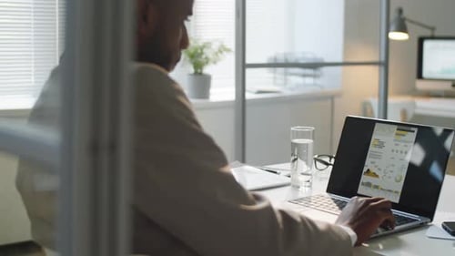 Afro-American Businessman Examining Charts on Laptop in Office