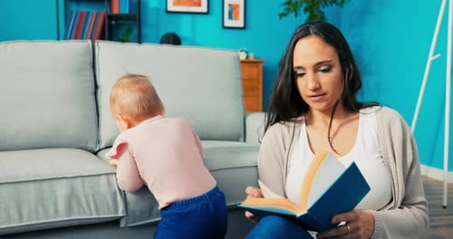 Woman Reading Book While Infant Plays Near Sofa